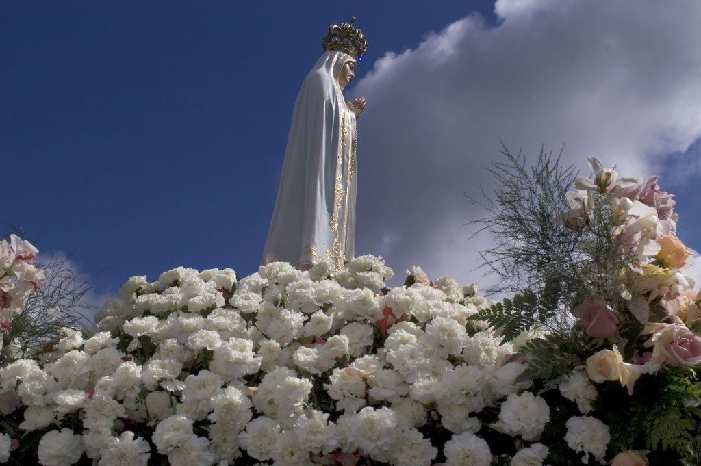Our Lady of Lourdes statue sitting on a bed of flowers.
